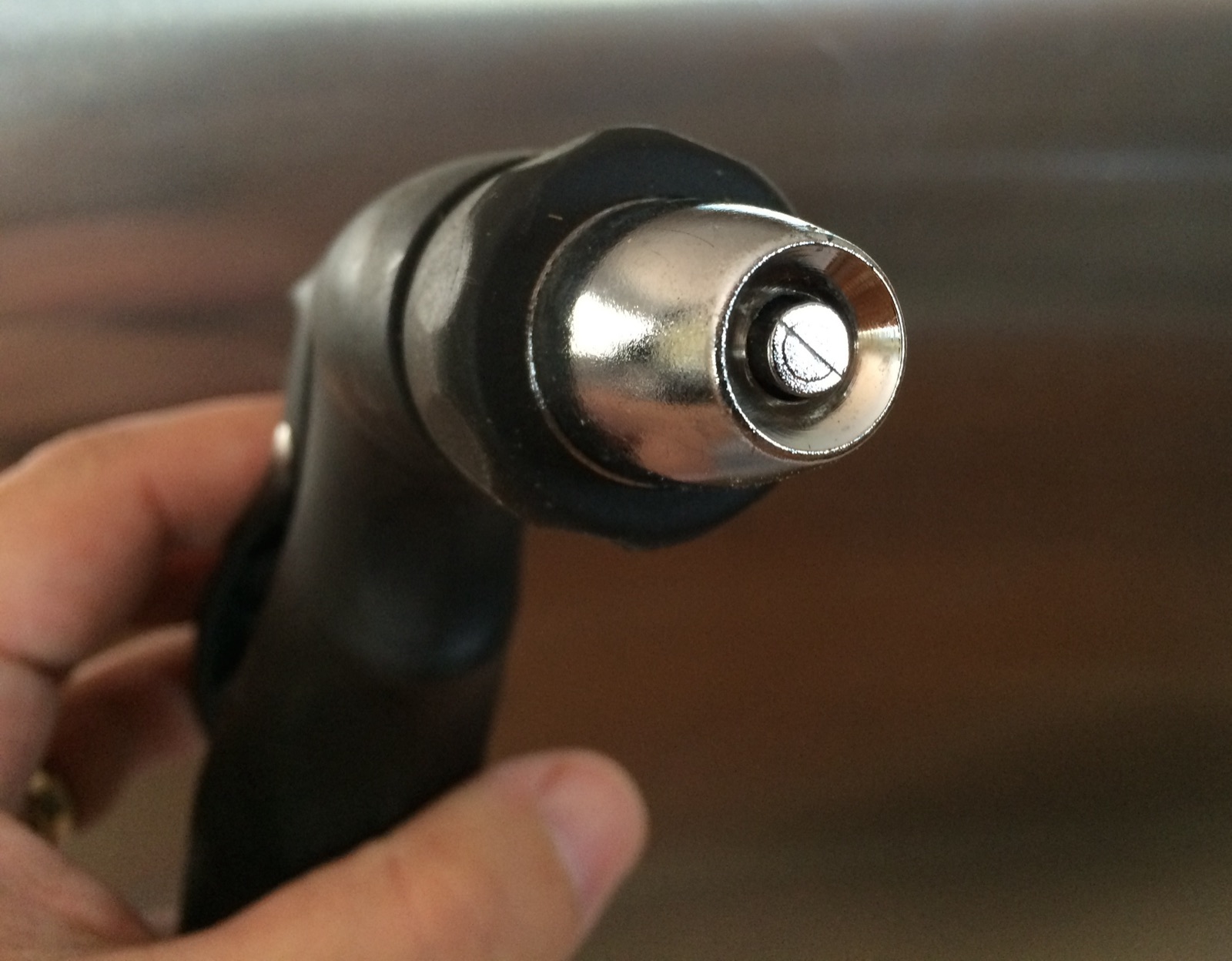 A hand holding an adjustable metal garden hose nozzle
