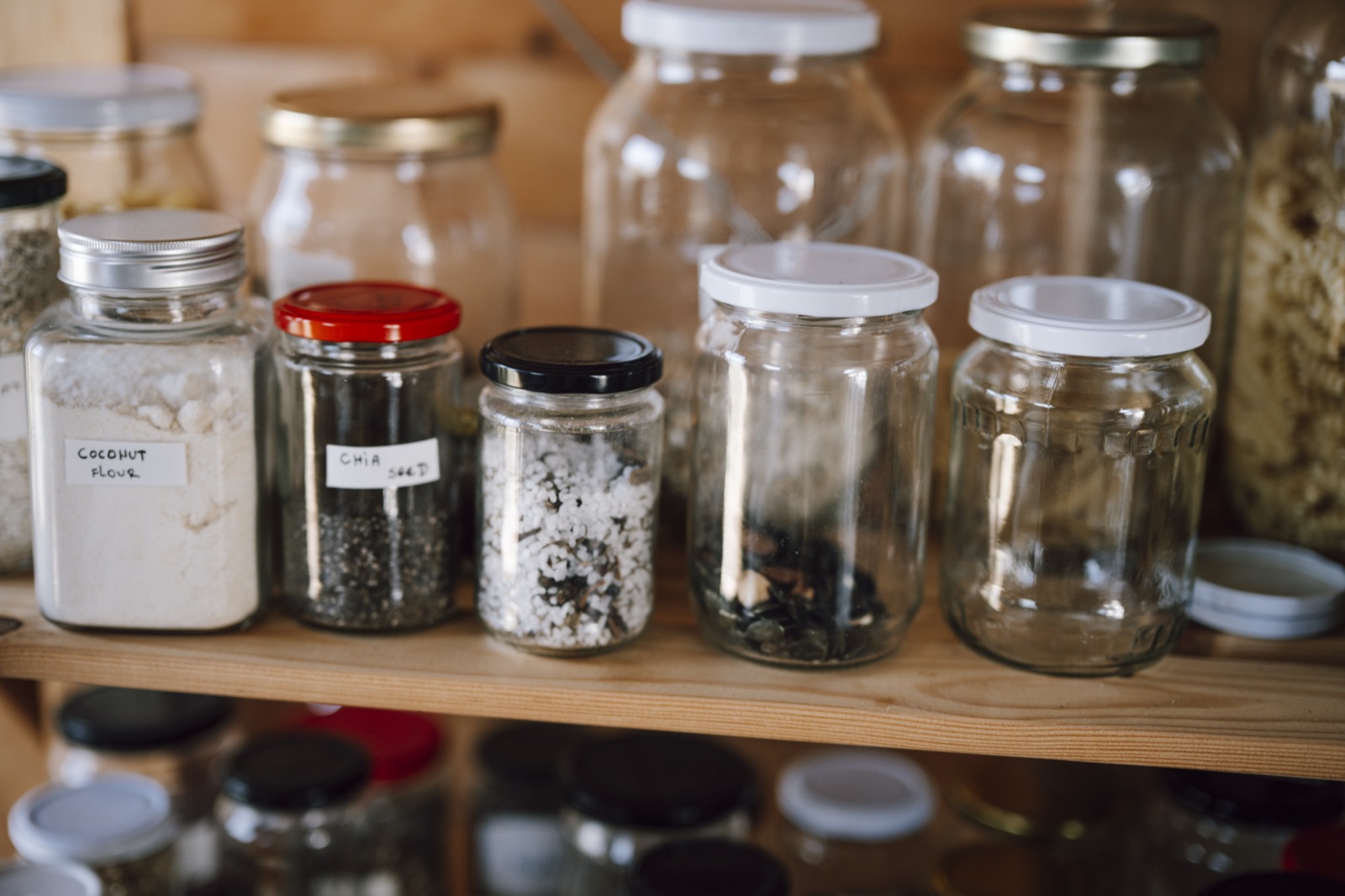 A pantry shelf of glass jars holding flour, chia seed, and other dry staples for long-term storage