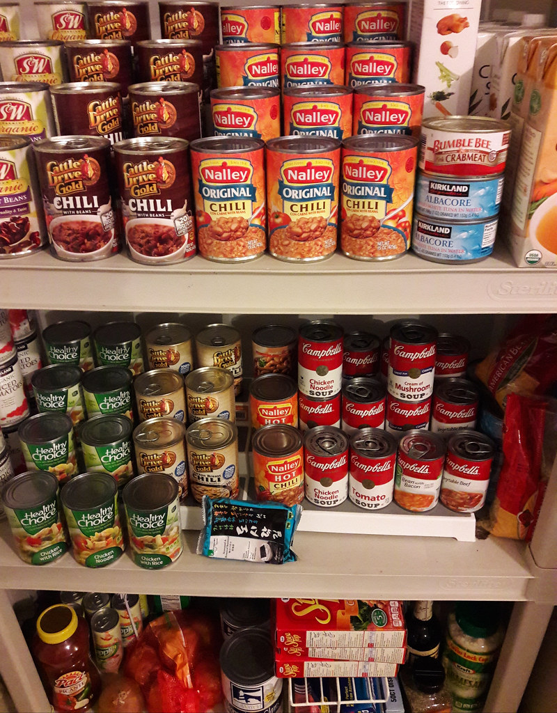 Pantry shelves stacked with canned chili, soup, tuna, and boxed staples