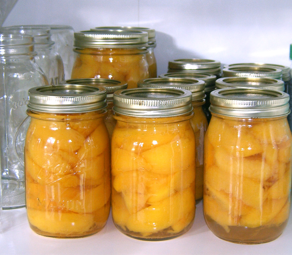 Rows of home-canned peaches in sealed Mason jars on a pantry shelf