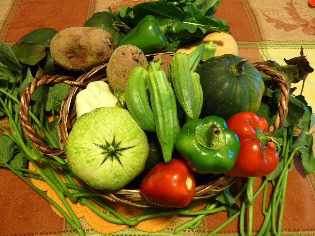 Woven harvest basket of okra, peppers, summer squash, and leafy greens on a kitchen table