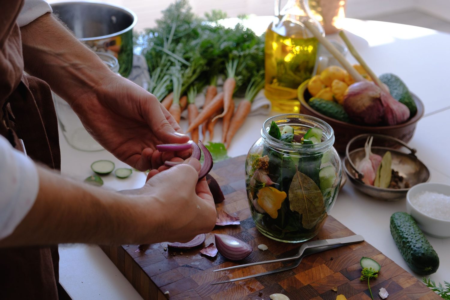 Hands packing fresh vegetables into a glass canning jar surrounded by garden produce